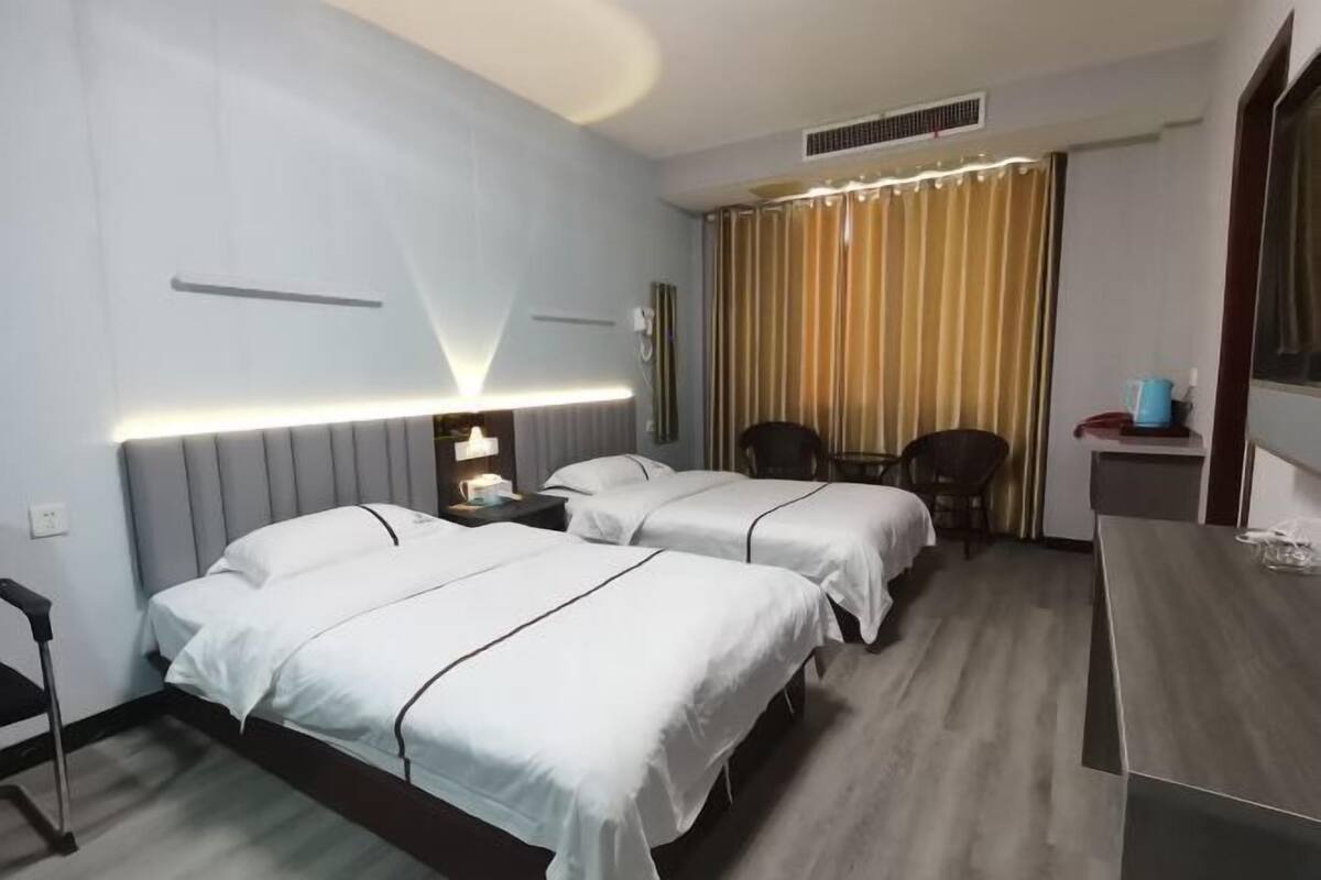 A hotel room with two beds, a desk, a chair, and a curtain.