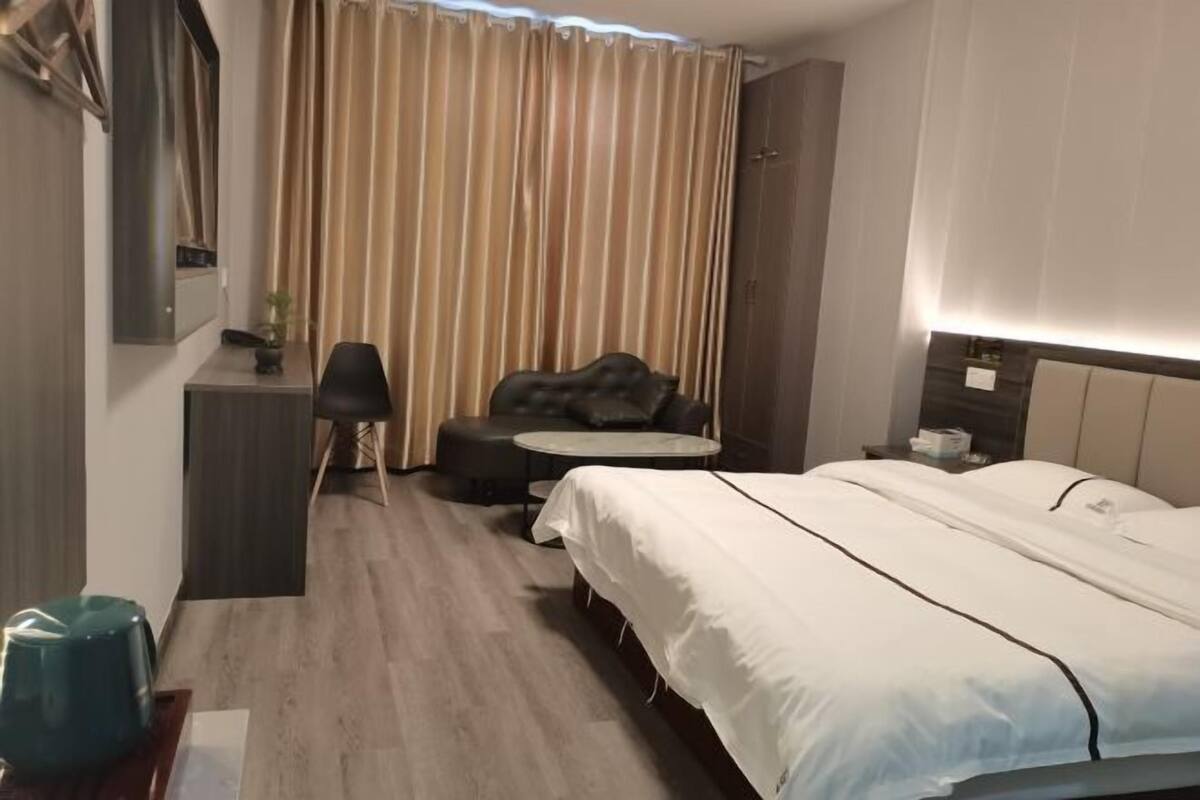 A hotel room with a bed, a desk, a chair, a sofa, and a curtain.