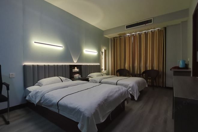 Habitación de hotel con dos camas, un escritorio, una silla y una ventana con cortinas.