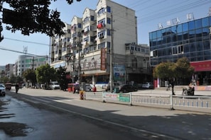 Un edificio de varios pisos con locales comerciales en la planta baja, un paseo peatonal y un cielo despejado.