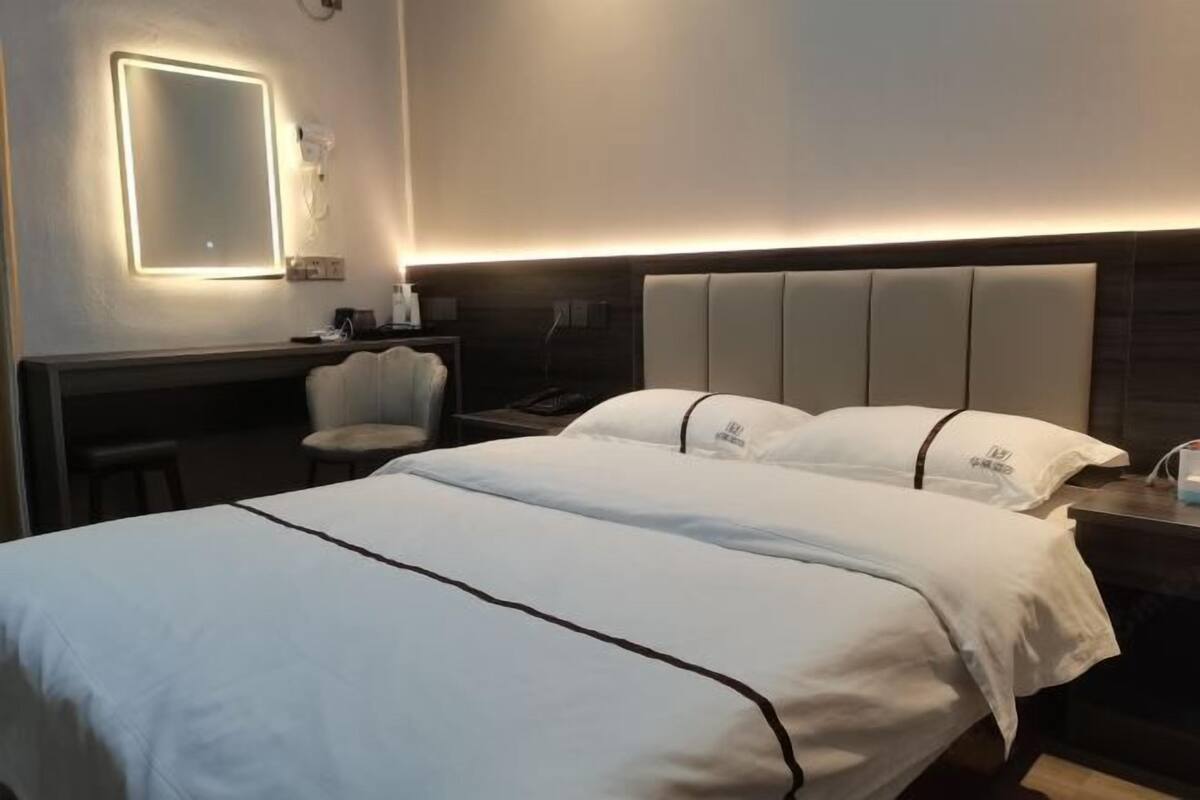 A hotel room with a bed, bedside tables, a chair, a desk, and a wall-mounted light.