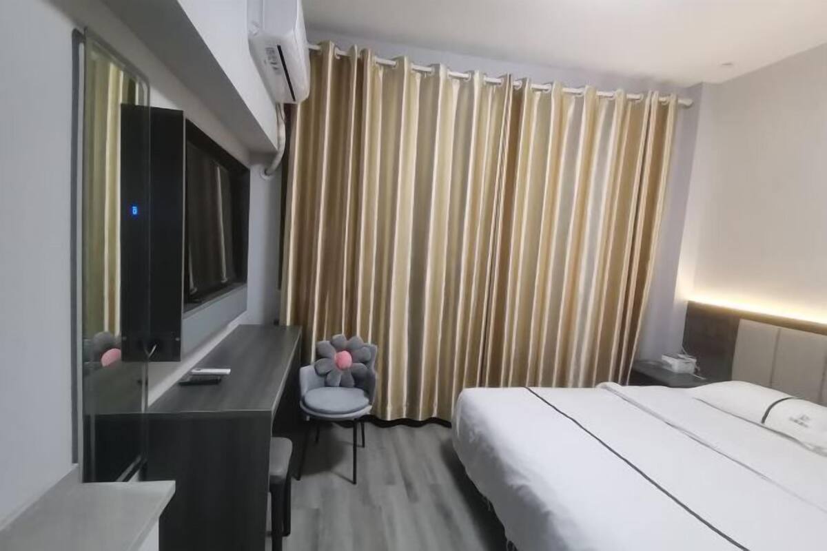 A hotel room with a bed, a desk with a chair, a mirror, and a curtain.