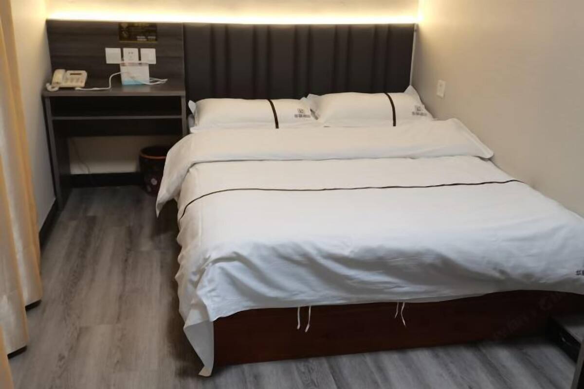 A neatly made bed with white bedding and a dark headboard in a hotel room.