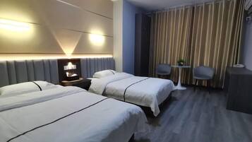 A hotel room with two beds, a bedside table, a small table with a plant, and a curtain-covered window.
