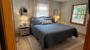 A bedroom with a bed, two bedside tables, a ceiling fan, a window with curtains, and a rug. - Serene waterfront home at Smith Mountain Lake in Huddleston, VA (Huddleston)