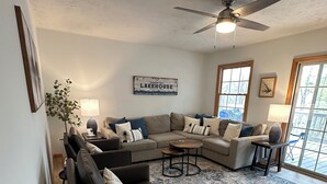 A living room with a sectional sofa, a small table, a floor lamp, a ceiling fan, and a rug. - Serene waterfront home at Smith Mountain Lake in Huddleston, VA (Huddleston)