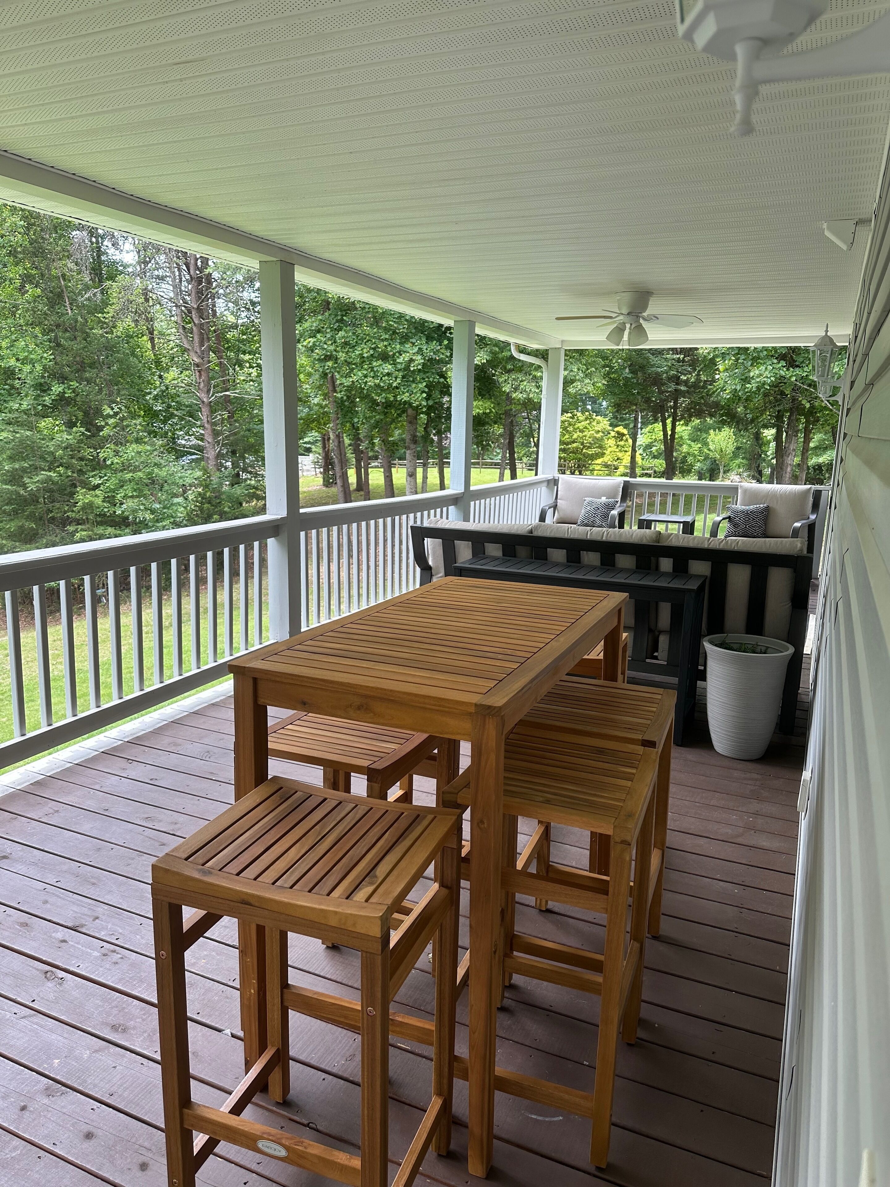 A covered porch with wooden furniture, including a table and chairs, and a bench with cushions.