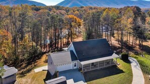 A house with a large garage, surrounded by a forest and mountains. - Serene waterfront home at Smith Mountain Lake in Huddleston, VA (Huddleston)