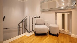 Una escalera con barandilla de metal, dos sillones tapizados, un radiador y una pared espejada.