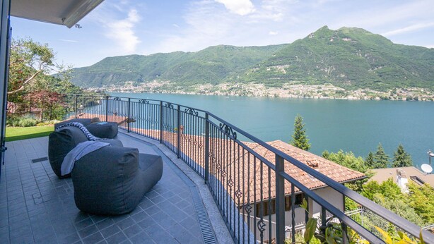 Un balcón con mobiliario exterior y vistas a un lago y montañas.