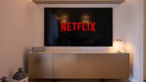 Una sala de estar moderna con un televisor de pantalla plana grande montado en la pared, mostrando el logotipo de Netflix.