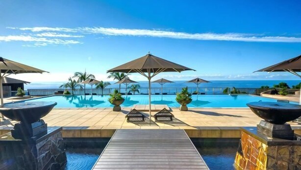Een zwembad met parasols, een houten terras en uitzicht op zee.