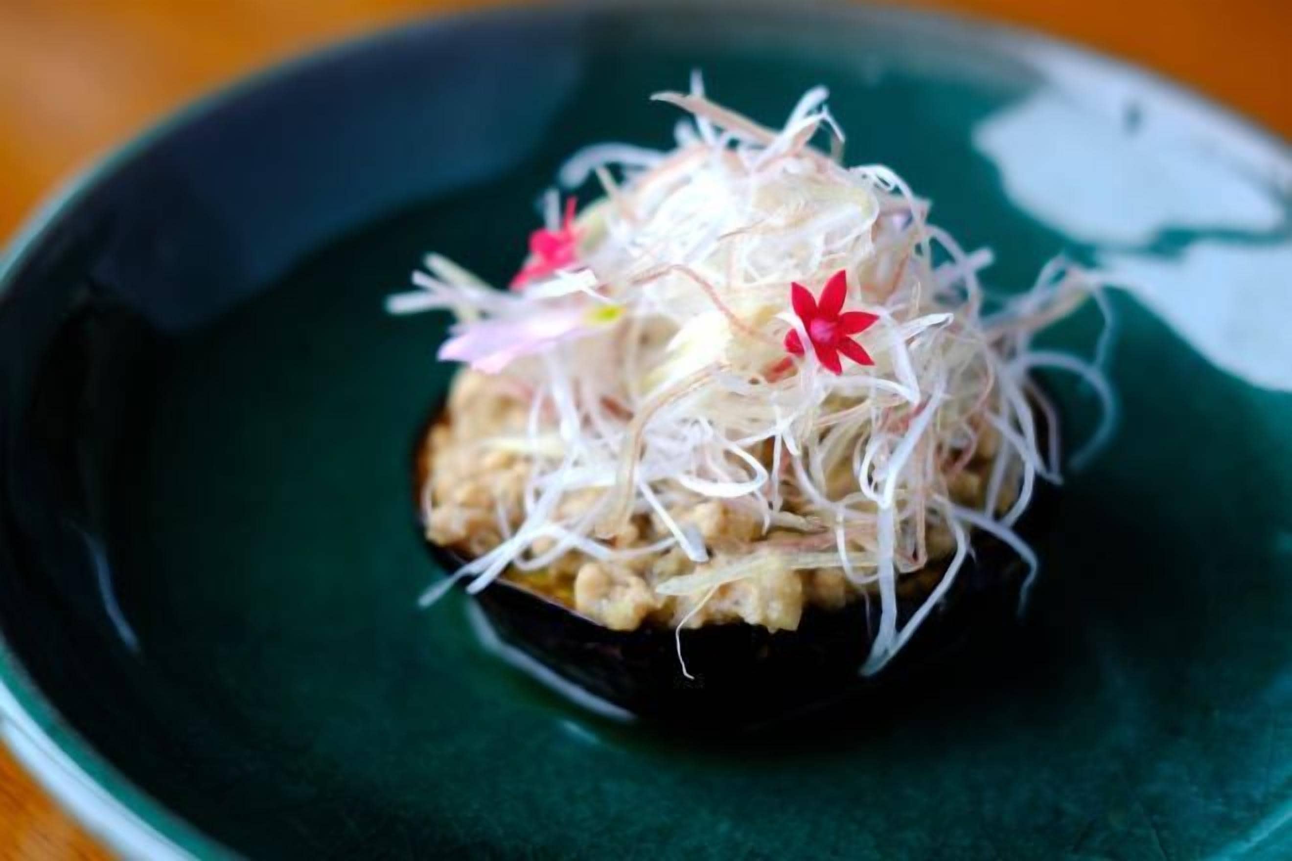 A dark green plate with a food item on top, possibly a mushroom or vegetable, and some white and red garnishes.