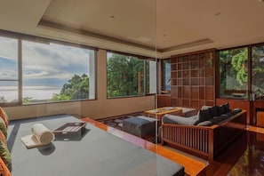 A modern living room with a large window, a sofa, a coffee table, and a bookshelf.