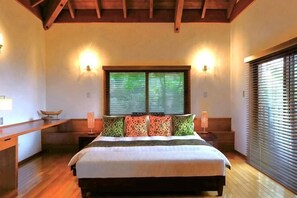 Un dormitorio con cama, mesitas de noche, una ventana con persianas y suelo de madera.