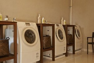 A row of front-loading washing machines on wooden stands with baskets underneath.