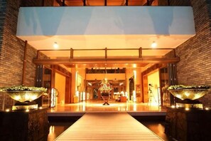 Een hotelentree met een houten looppad, grote verlichte plantenbakken en een modern interieur.