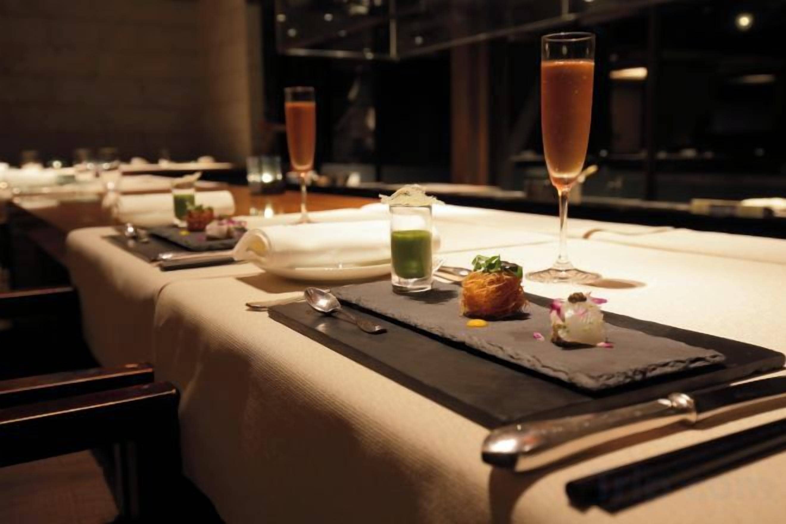 A restaurant setting with tables set for dining, each with a glass of beverage and a small plate of food.