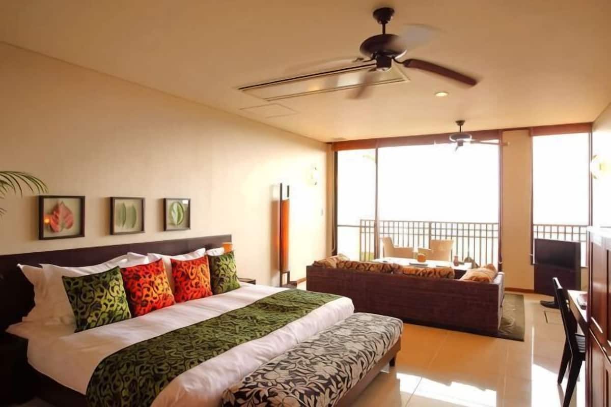 Une chambre avec un lit, un ventilateur de plafond, un balcon avec vue et un canapé.