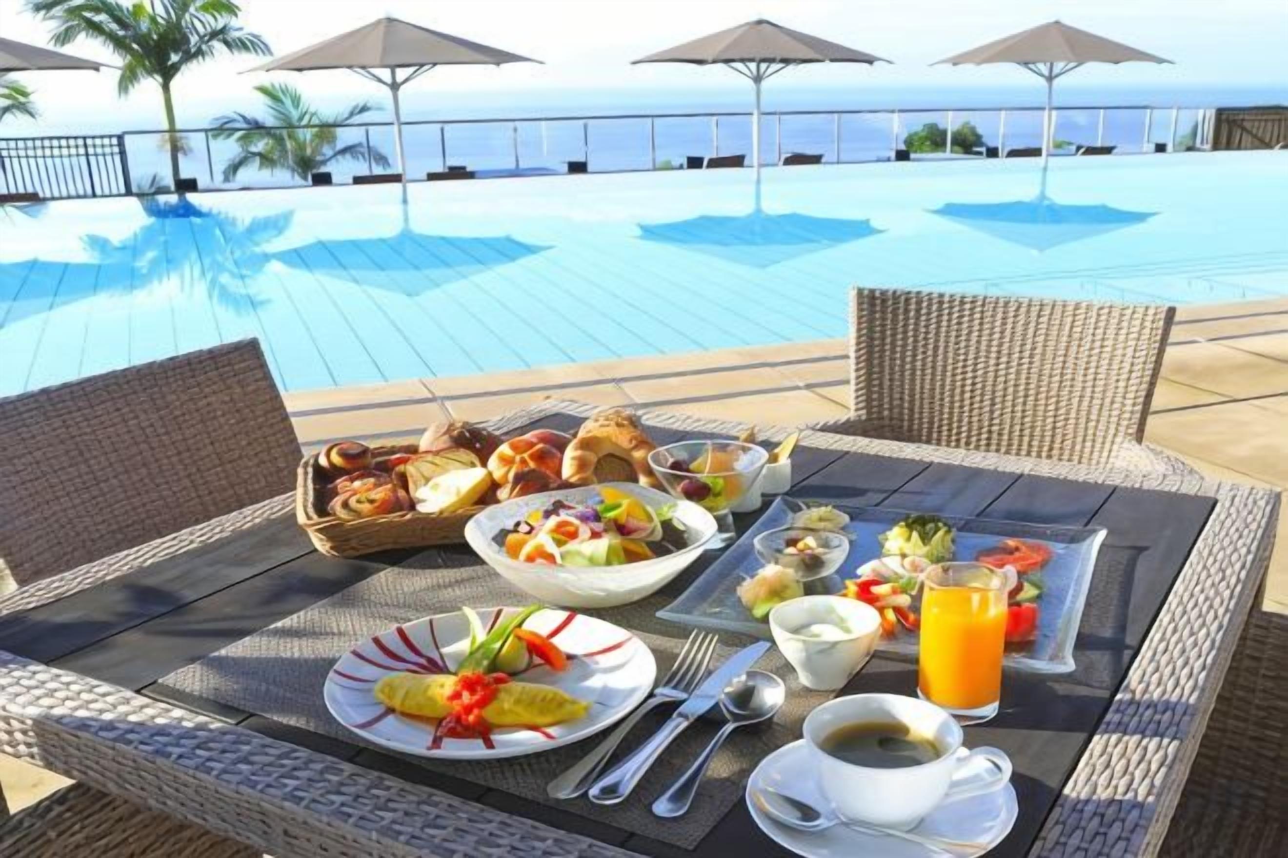 A dining table with breakfast items, a poolside view, and umbrellas.