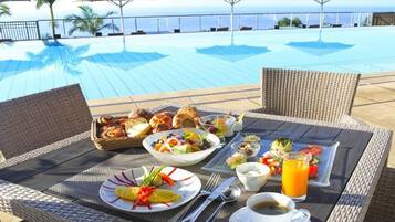 A dining table with breakfast items, a poolside view, and umbrellas.