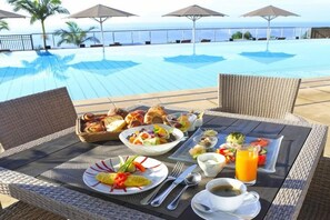Une table à manger avec des aliments pour le petit-déjeuner, une vue sur la piscine et des parasols.