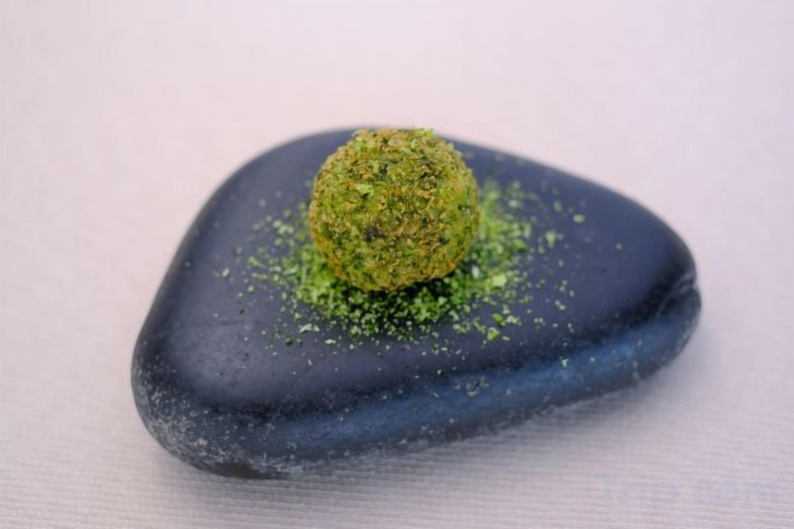 A single green-colored spherical object on a dark blue surface.