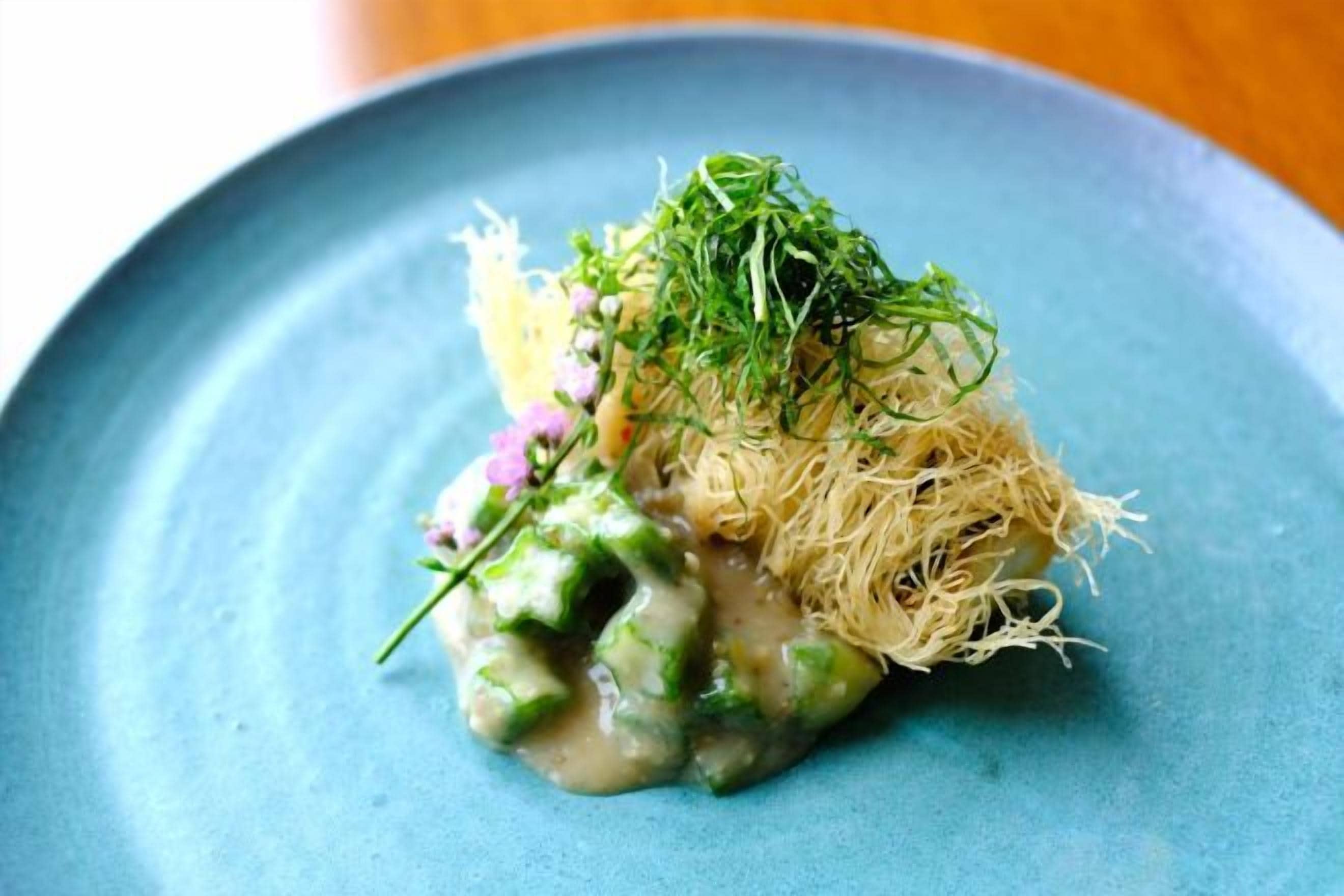A dish with noodles, greens, and a creamy sauce on a blue plate.