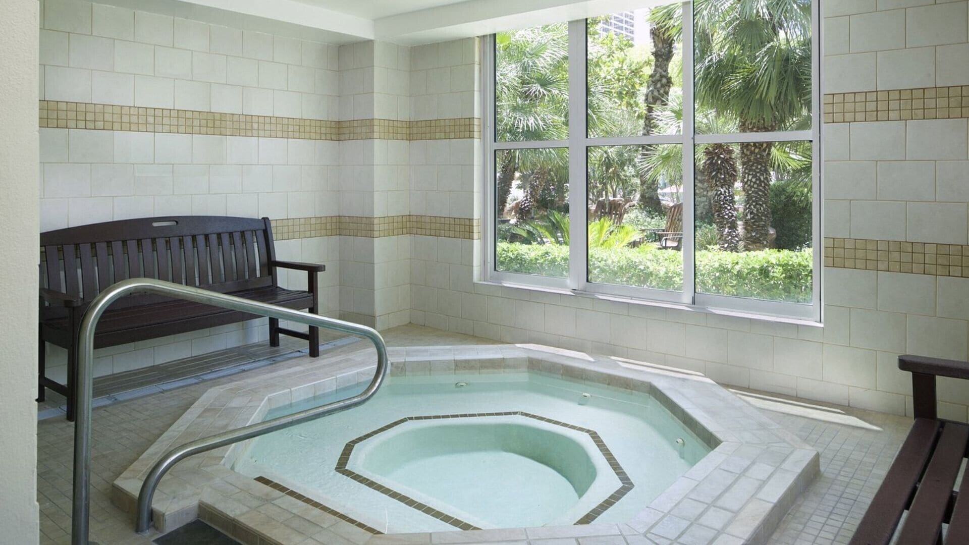 Un cuarto de spa con hidromasaje, una banca y una ventana con vistas a la vegetación.