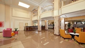 A spacious lobby with a reception desk, seating areas, and a second-floor balcony.