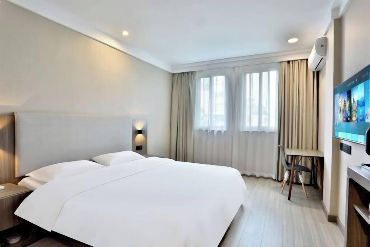 Ein Hotelzimmer mit einem großen Bett, einem Schreibtisch mit Stuhl, einem Flachbildfernseher und einem Fenster mit Vorhängen.