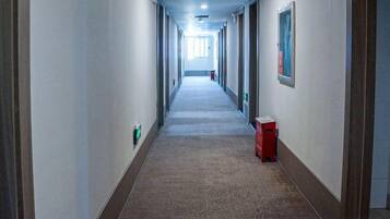 A long, narrow hotel corridor with doors on both sides, a red trash bin, and a framed picture on the right wall.