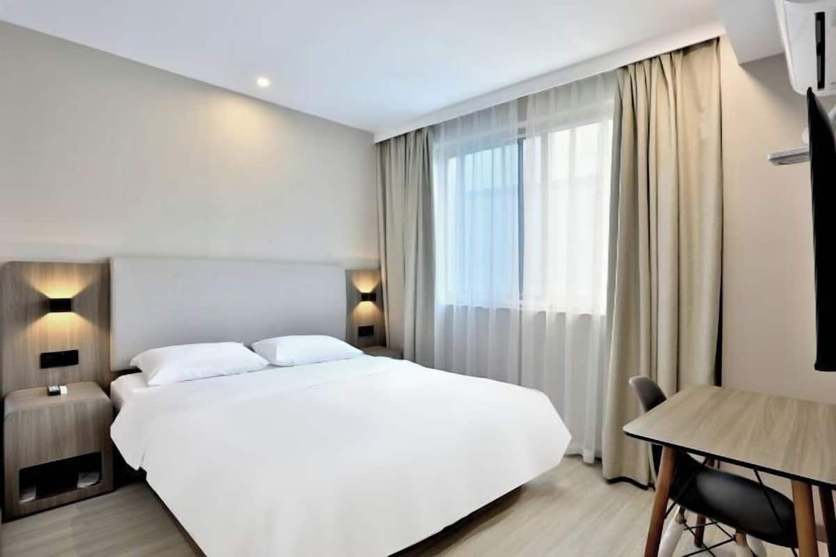 Ein modernes Hotelzimmer mit einem großen Bett, Nachttischen mit Lampen, einem Schreibtisch und einem Stuhl.