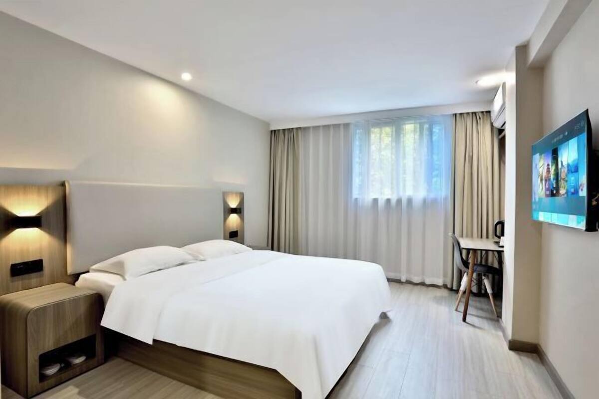 Ein modernes Hotelzimmer mit einem großen Bett, Nachttischen, einem Schreibtisch und einem Fernseher.