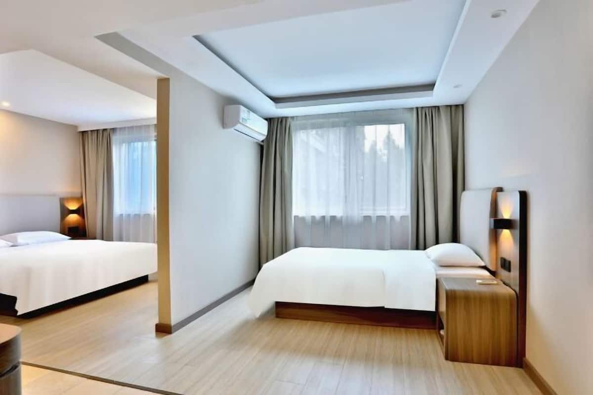 Ein Hotelzimmer mit zwei Betten, einem großen Fenster mit Vorhängen, einer Wand-Klimaanlage und einem Nachttisch mit Lampe.