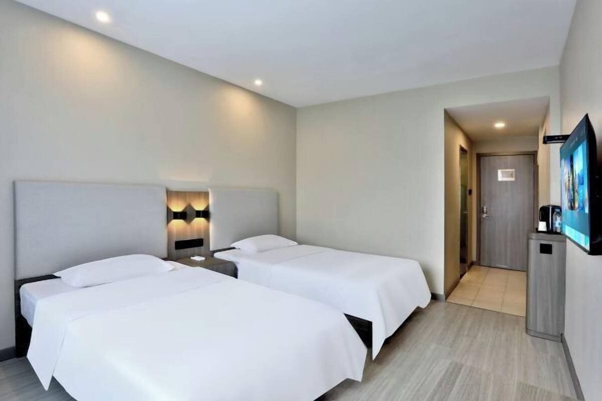 Ein Hotelzimmer mit zwei Betten, einem Fernseher und einer kleinen Küchenzeile.