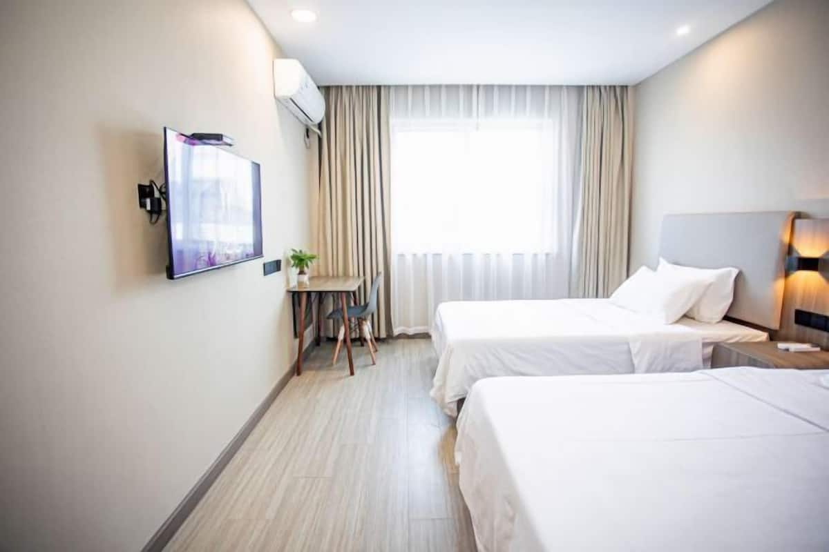 Ein Hotelzimmer mit zwei Betten, einem Schreibtisch, einem Fernseher und einem fenster mit Vorhängen.