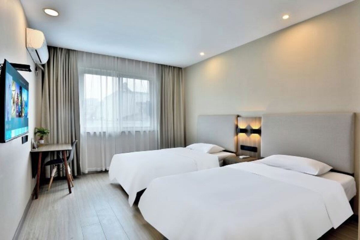 Une chambre d’hôtel avec deux lits, un bureau, une télévision et une fenêtre avec des rideaux.