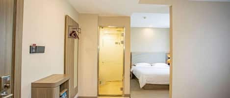 A hotel room with a bed, a bedside table, a wardrobe, and a door leading to a bathroom.