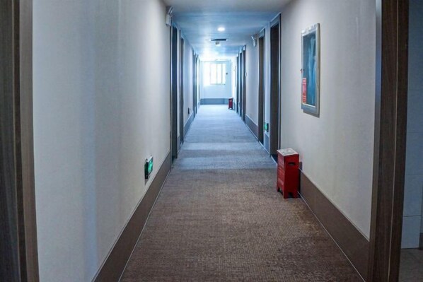 A long, narrow hallway with a carpeted floor, doors on both sides, and a fire extinguisher on the right wall.