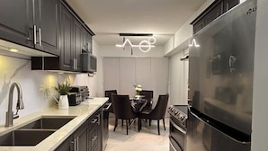 A modern kitchen with dark cabinets, a stainless steel refrigerator, and a dining area with a table and chairs. - Super Luxury House with 3 Bedrooms, 1-1/2 Washrooms, Basement and Free Parking (Toronto)