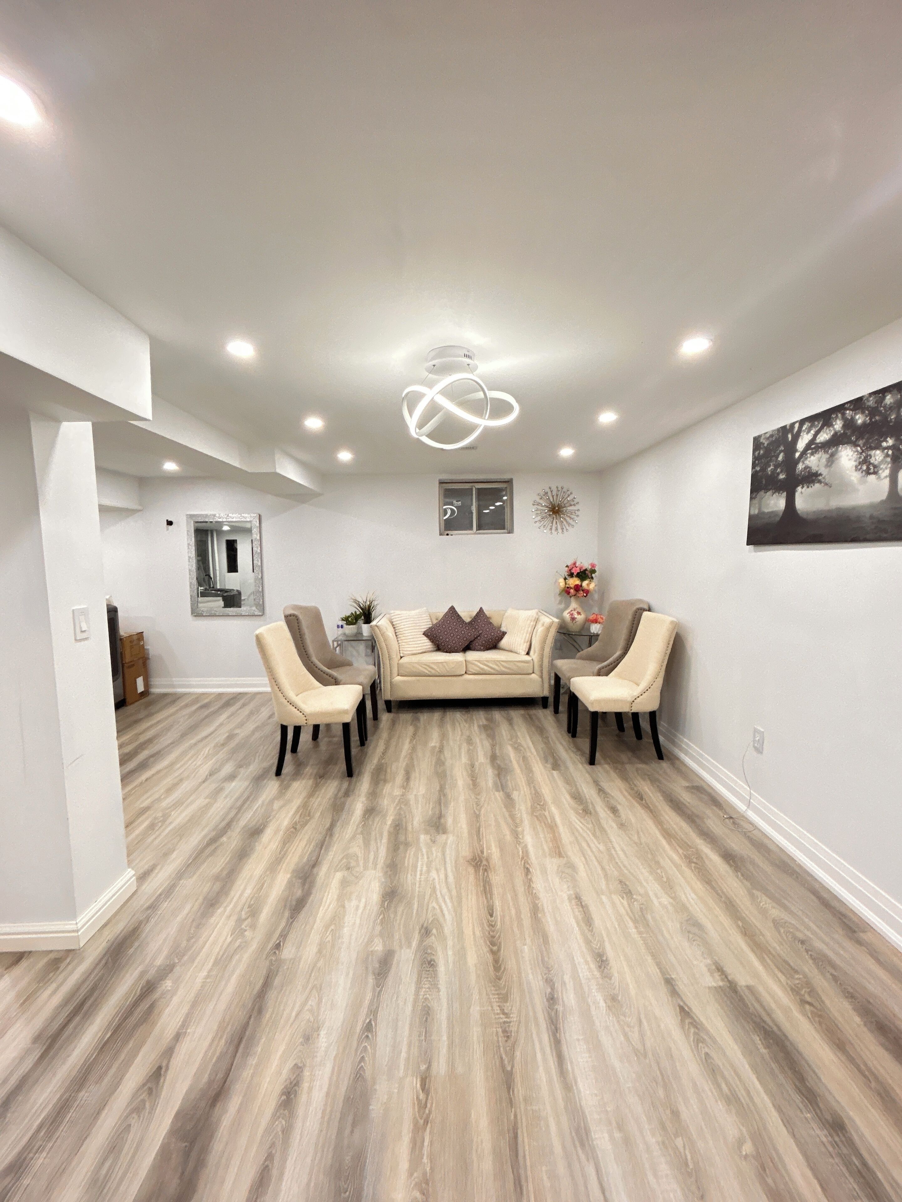 A spacious room with a wooden floor, a beige sofa set, and a modern ceiling light fixture.