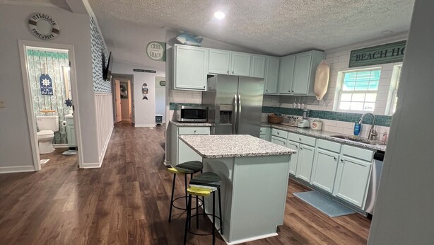 A spacious kitchen with a central island, wooden flooring, and light-colored cabinets.