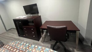 Ein kleines Zimmer mit Schreibtisch, Stuhl, Fernseher und Kleiderschrank.