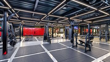 Un gimnasio moderno con diversos equipos de levantamiento de pesas, taquillas rojas y un lema motivacional en la pared.