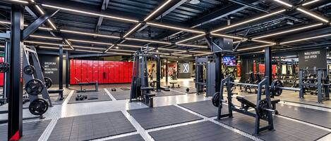 A modern gym with various weightlifting equipment, red lockers, and a motivational slogan on the wall.