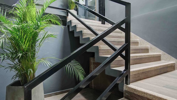 Eine moderne Treppe mit schwarzer Metallgeländer und beigefarbenen Stufen, umgeben von Topfpflanzen.