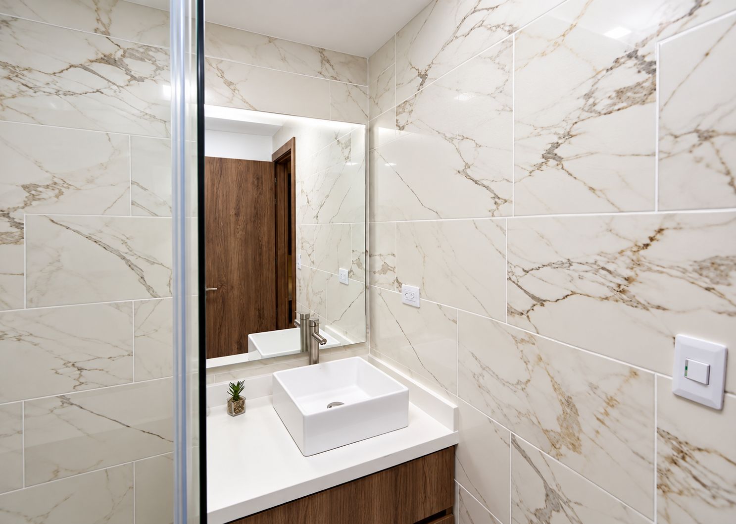 A bathroom with a white marble tiled wall, a white sink, and a wooden cabinet.
