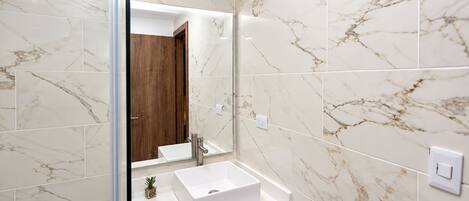 A bathroom with a white marble tiled wall, a white sink, and a wooden cabinet.