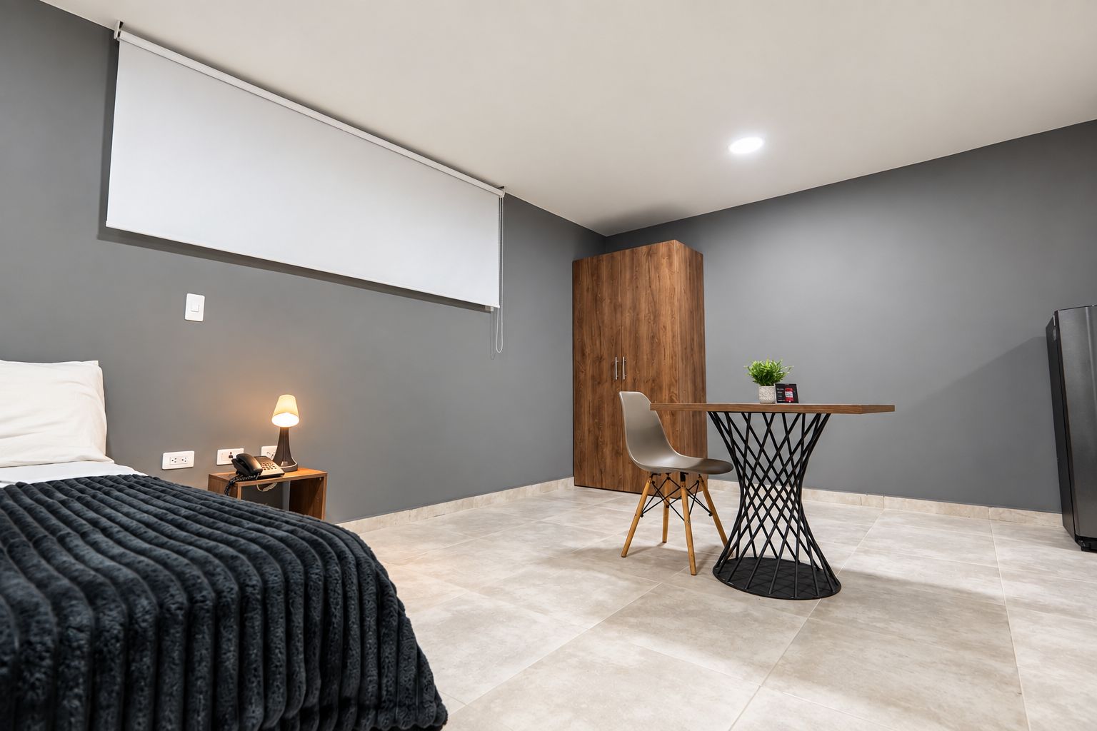 A modern bedroom with a bed, bedside table, lamp, and a wooden wardrobe.